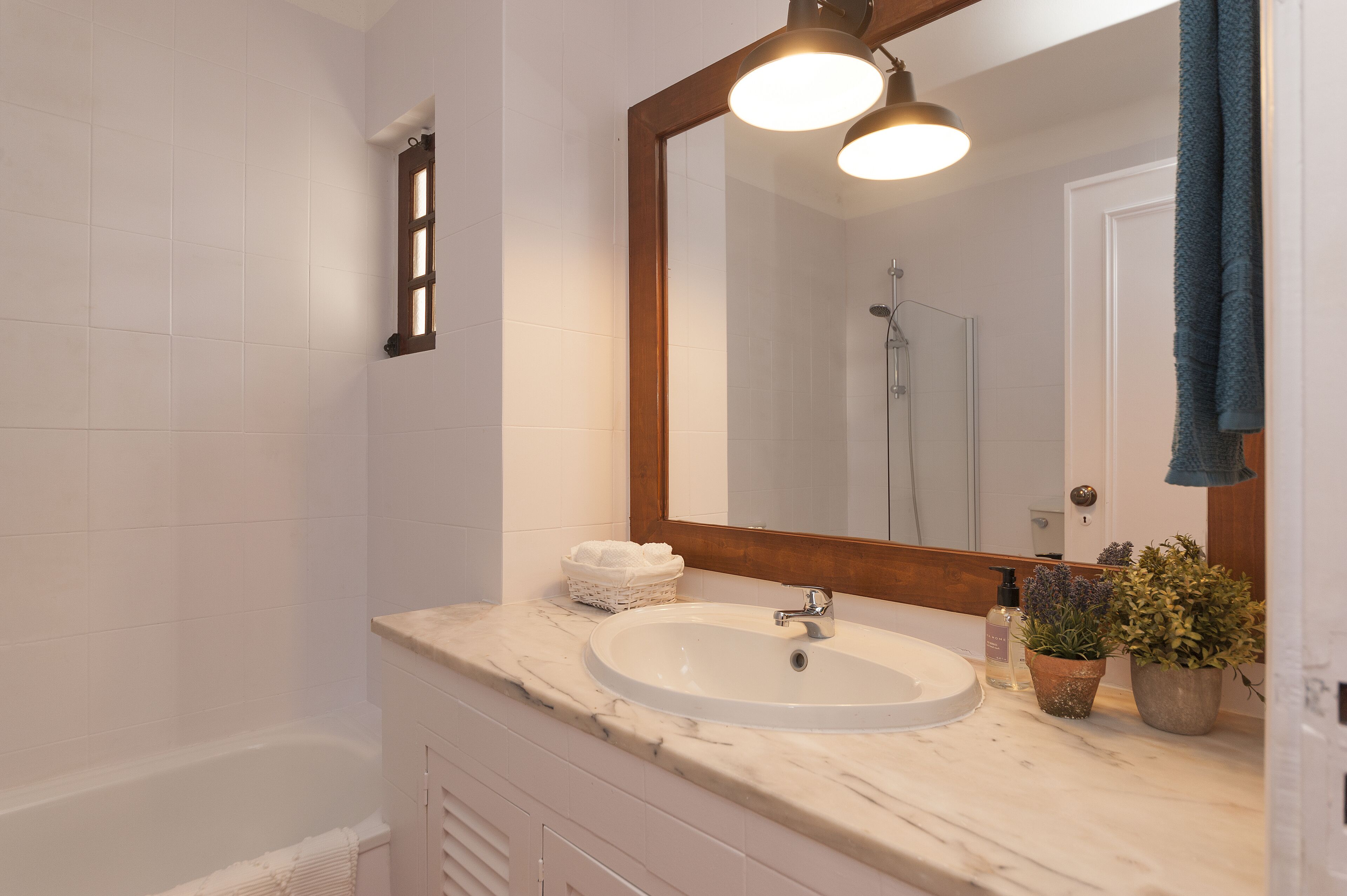 A bathroom with a white sink, a large mirror, and a shower. There are towels and plants on the counter.