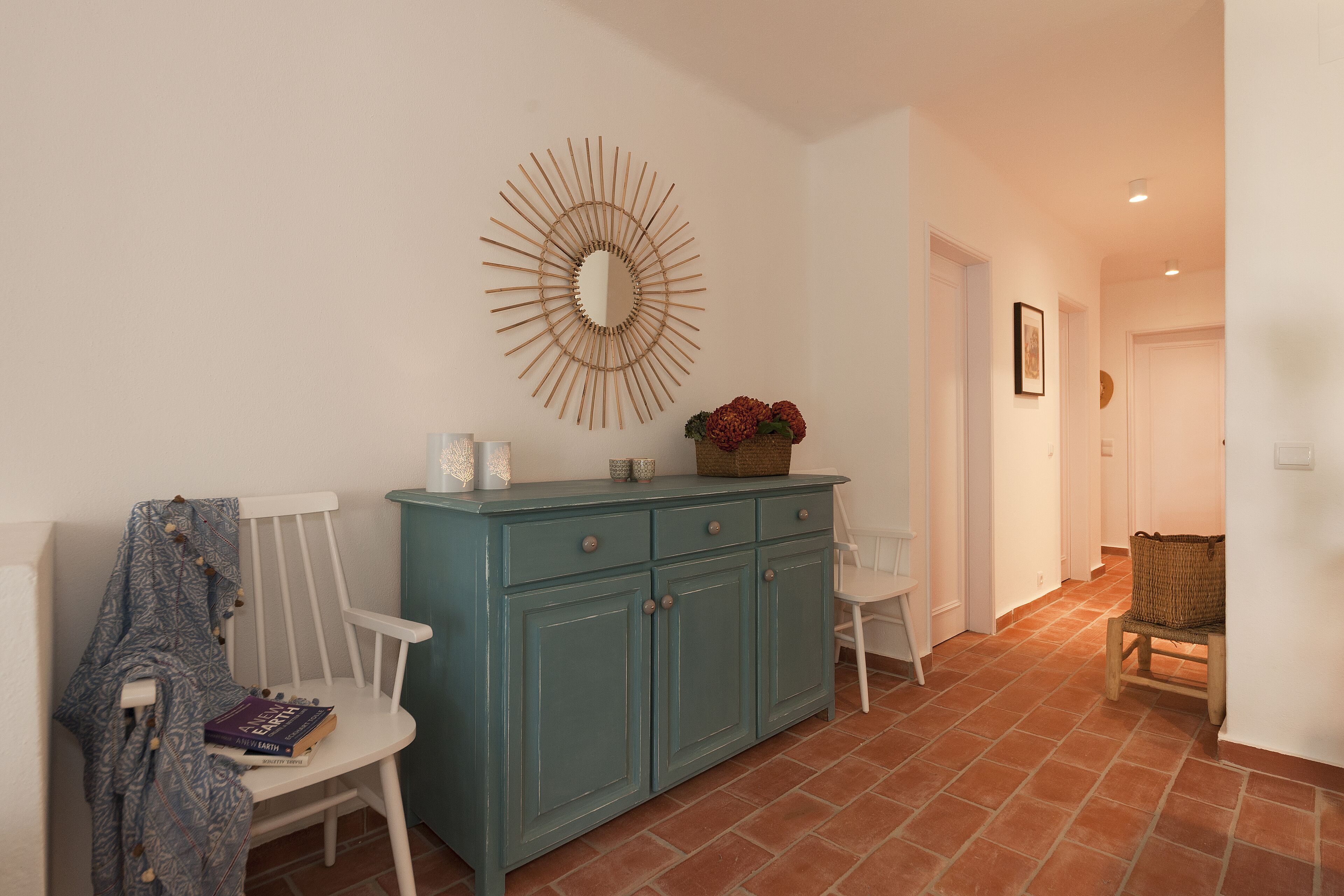 A hallway with a teal cabinet, white chairs, a mirror, and a wicker basket.