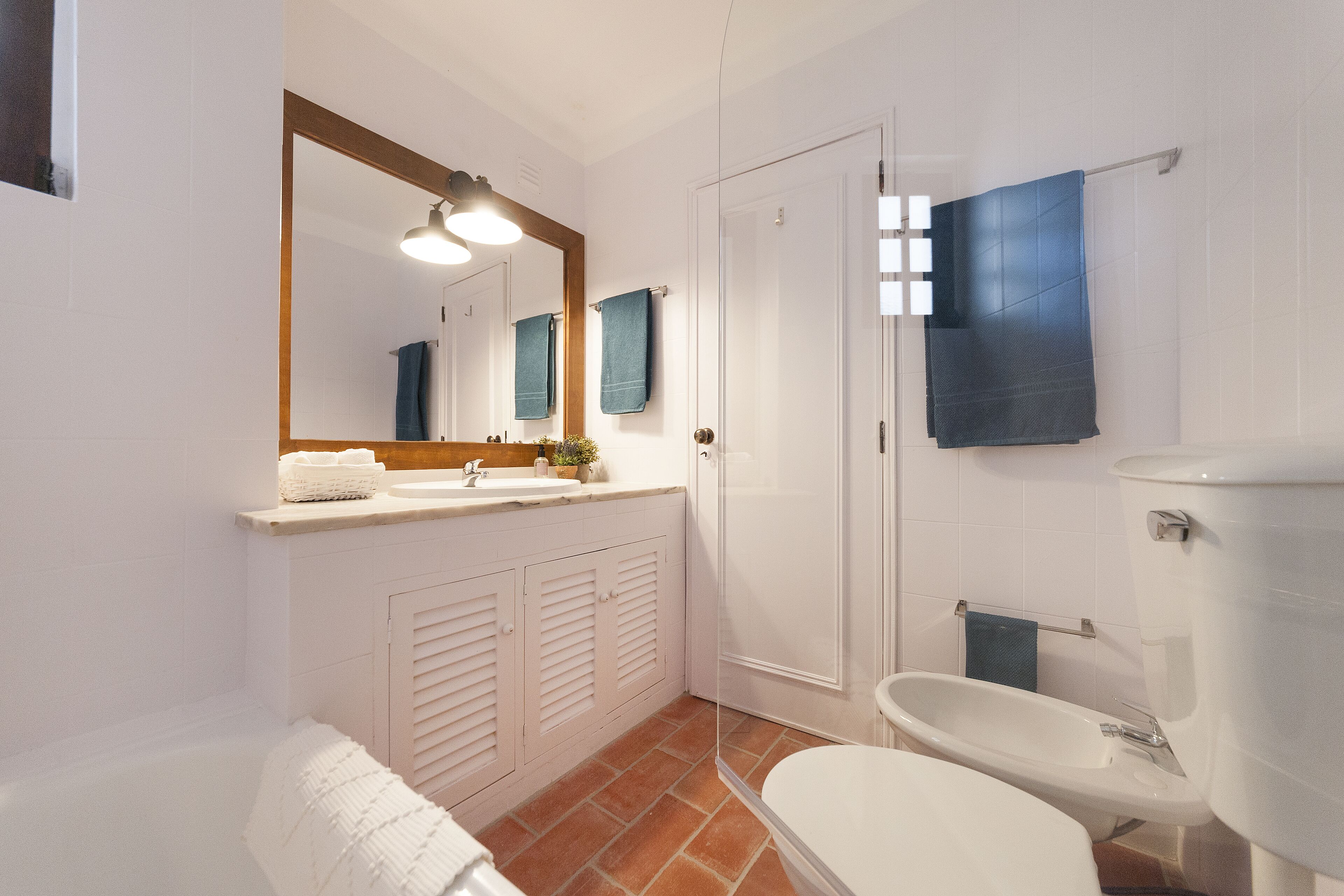 Une salle de bain avec un lavabo blanc, un miroir et des toilettes. On y trouve également un porte-serviettes et un espace douche.