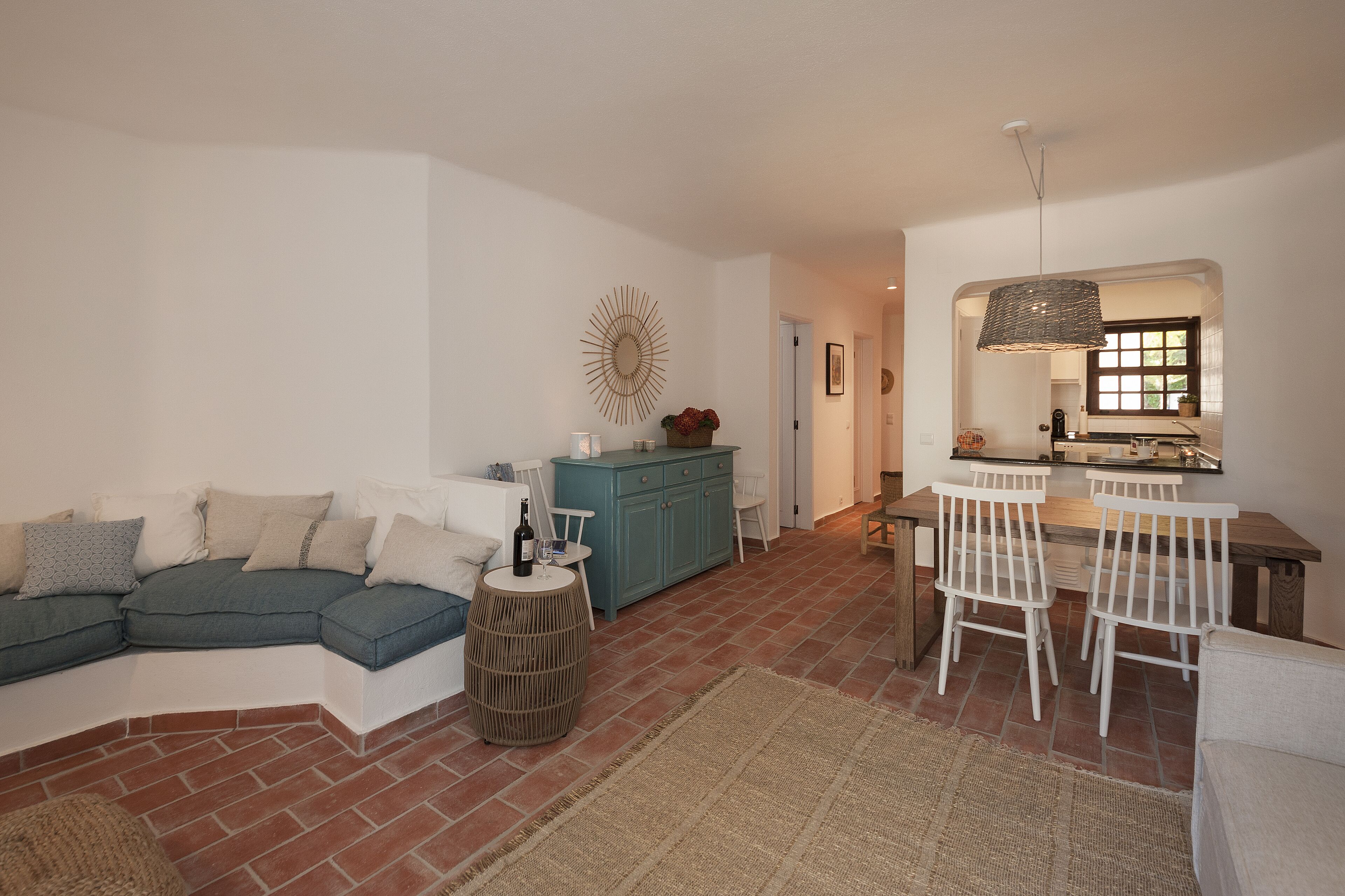 Een moderne woonkamer met een hoekbank, een eetgedeelte met witte stoelen, en een keuken op de achtergrond.