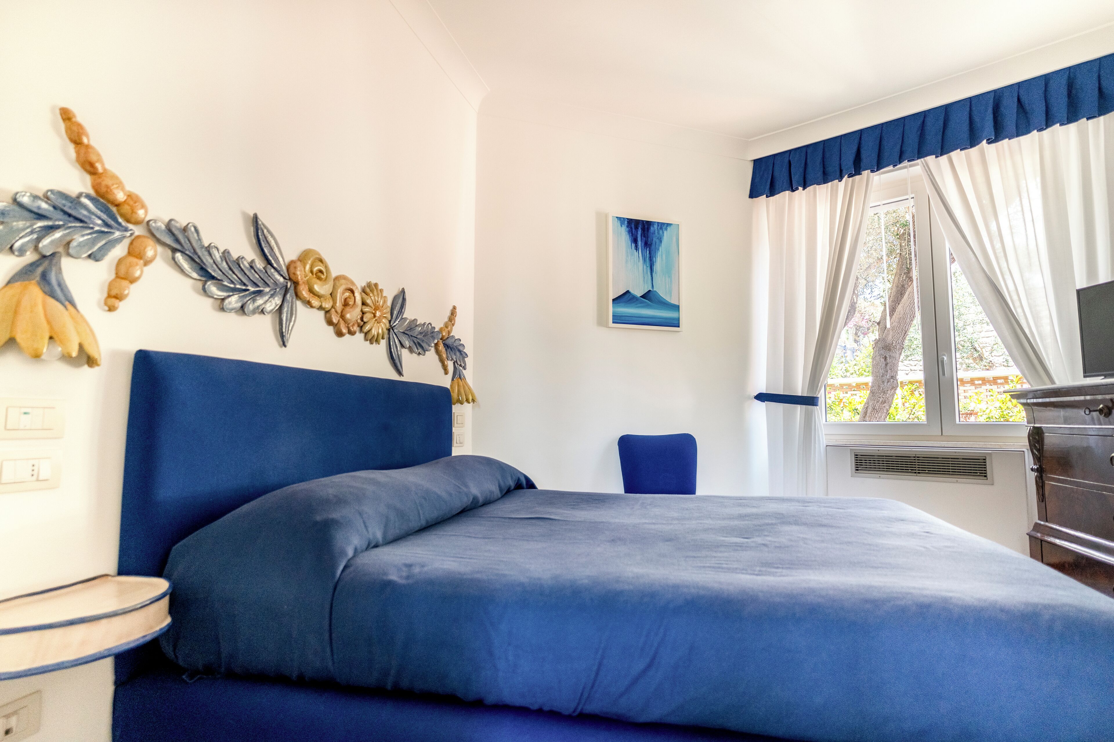 Un dormitorio con una cama grande, un aparador, una silla y un ventanal con cortinas.