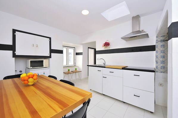 A compact kitchen with white cabinets, a microwave, a sink, and a wooden dining table with chairs.