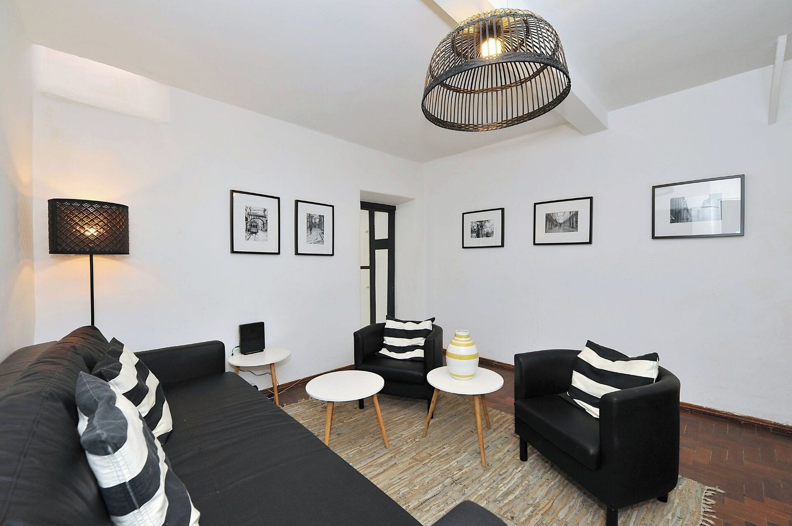 Una sala de estar moderna con un sofá negro, dos sillones, una mesita y una lámpara de pie. Hay cuadros enmarcados en la pared.