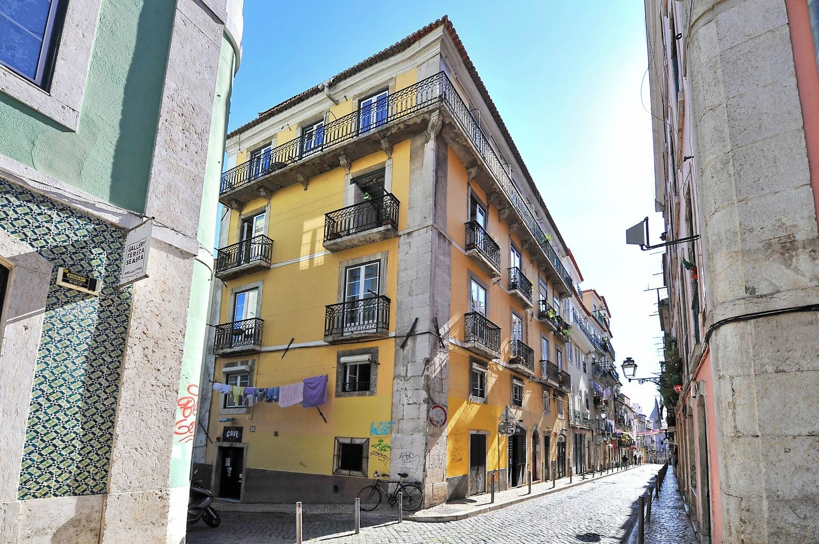 A narrow street with buildings featuring balconies and a tiled facade.