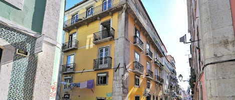 A narrow street with buildings featuring balconies and a tiled facade.