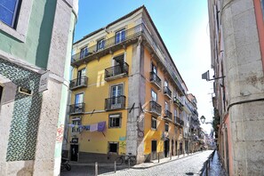 A narrow street with buildings featuring balconies and a tiled facade.