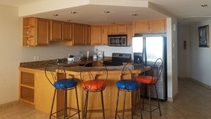 A kitchen with wooden cabinets, a microwave, a stove, a refrigerator, and three bar stools with blue and red cushions. - !!!!!!  LA JOLLA DEL MAR ROSARITO SHORES. !!!!! (Playas Rosarito)