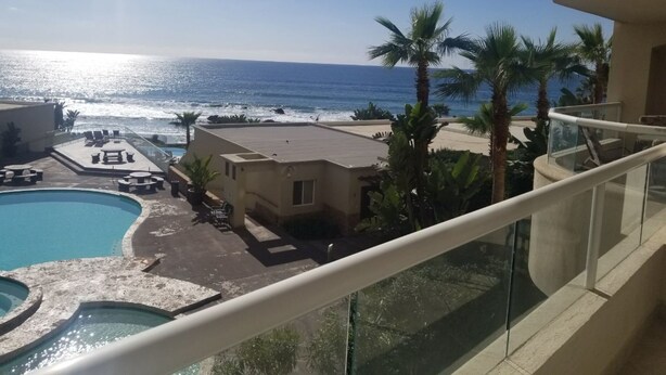 A pool area with a view of the ocean, palm trees, and a building with a balcony. - !!!!!!  LA JOLLA DEL MAR ROSARITO SHORES. !!!!! (Playas Rosarito)