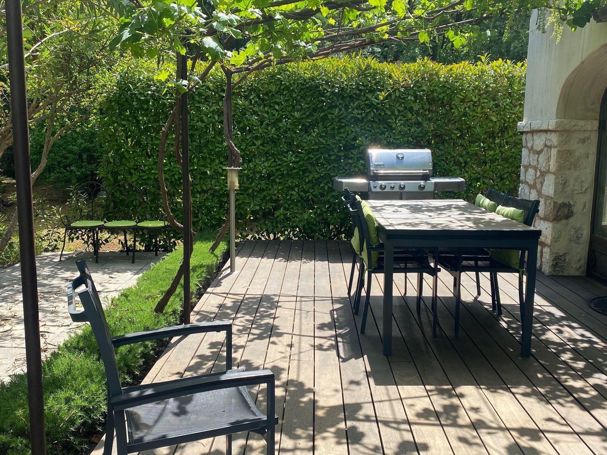 Une terrasse en bois avec un barbecue, des sièges d’extérieur et une haie en arrière-plan.