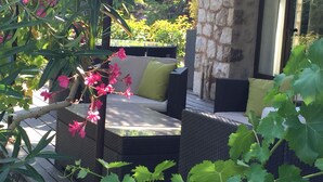 An outdoor seating area with wicker furniture and cushions, surrounded by lush greenery and flowering plants. - Comfortable, quiet, spacious apartment, lush garden, Nice hinterland  (Roquefort-Les-Pins)