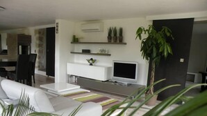 A modern living room with a white sofa, a flat-screen TV, a coffee table, and a large potted plant. - Comfortable, quiet, spacious apartment, lush garden, Nice hinterland  (Roquefort-Les-Pins)