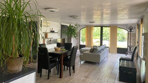 A spacious living area with a dining table, black chairs, a sofa, and a large potted plant. - Comfortable, quiet, spacious apartment, lush garden, Nice hinterland  (Roquefort-Les-Pins)