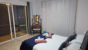 Habitación de hotel con cama, escritorio, silla y puerta corrediza de vidrio que da a un balcón.