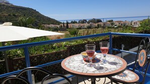 Un balcón con una mesa, dos vasos de bebida y vistas a un pueblo costero y al mar.