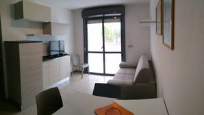 A compact living space with a kitchenette, a sofa, a dining table, and a TV. - Flat with balcony and shared pool (Lignano Sabbiadoro)