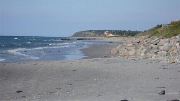 A beach with a rocky shoreline, a small building, and a clear sky. - Holiday house close to the beach  (Hundested)