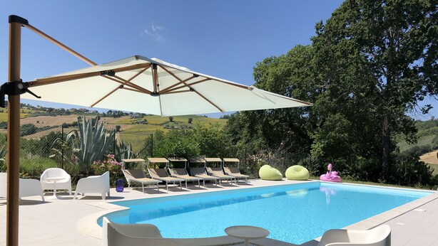 A swimming pool with lounge chairs and a canopy, surrounded by greenery and hills. - Very private, spacious, rural, detached villa with a pool, nestled between the sea and the mountains (Monte San Pietrangeli)