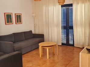 Olohuoneessa on sohva, pyöreä puinen pöytä ja kaksi kehystettyä kuvaa seinällä.