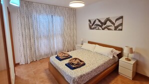 A neatly arranged bedroom with a bed, a bedside table, a lamp, and a window with curtains. - Semi-detached Villa, 2 bedrooms, 2 bathrooms, private pool, WiFi, parking (Playa Blanca)