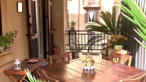 Een houten eettafel met stoelen, een potplant en een lantaarn op een balkon met uitzicht op gebouwen.