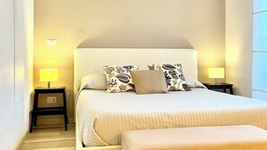 Een slaapkamer met een groot bed, twee nachtkastjes met lampen, een bankje en een gewelfde deuropening.