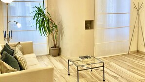 Een moderne woonkamer met een bank, een glazen salontafel, een potplant en een vloerlamp.