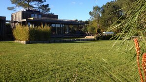 A modern house with a large glass facade, a wooden deck, and a well-maintained lawn. - BRIGHT 250m² ARCHITECT-DESIGNED VILLA OPEN TO THE OUTDOORS WITH PRIVATE POOL (Messanges)