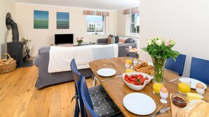 A cozy living room with a sofa, a dining table set with breakfast, and a fireplace. - Mousehole Cottage: sea views, parking & close to village centre, dog friendly. (Mousehole)