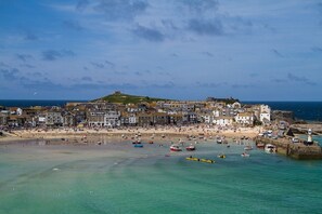 A coastal town with a historic fort on a hill, a sandy beach, and a marina with boats.