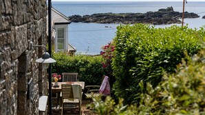 A stone building with a wooden table and chairs, a lamp, and a view of the sea. - Mousehole Cottage: sea views, parking & close to village centre, dog friendly. (Mousehole)