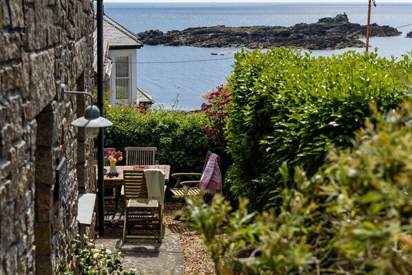 A stone building with a wooden table and chairs, a lamp, and a view of the sea.