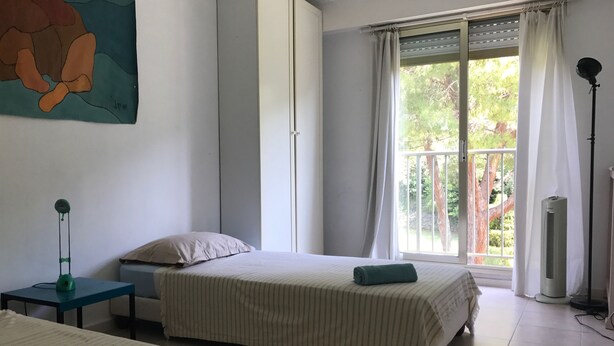 A room with two beds, a standing lamp, a window with curtains, and a painting on the wall. - Sorry, not available this year - Sorry, apartment not available this year. (Antibes)