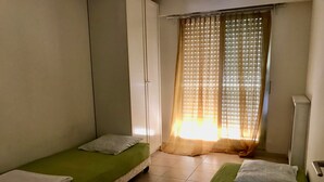 A room with two single beds, each with a pillow and a folded towel. There is a window with sheer curtains allowing natural light. - Sorry, not available this year - Sorry, apartment not available this year. (Antibes)