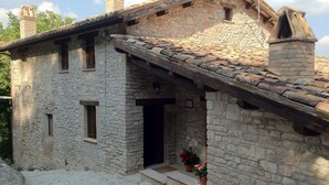 A stone building with a tiled roof, a wooden door, and a small porch with potted plants. - Colle di Pietra - Colle di PIetra (Cessapalombo)