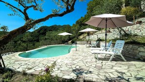 A poolside area with stone flooring, white lounge chairs, and umbrellas. - Colle di Pietra - Colle di PIetra (Cessapalombo)