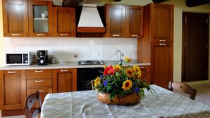 A kitchen with wooden cabinets, a microwave, a coffee maker, and a sink. There is a table with a floral centerpiece. - Colle di Pietra - Colle di PIetra (Cessapalombo)