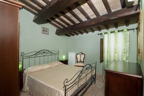 A bedroom with a bed, a nightstand, a chair, a desk, and a window with curtains.