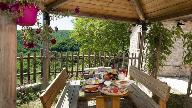 An outdoor wooden table with benches, surrounded by a stone wall and a wooden fence, with a view of a green landscape in the background. - Colle di Pietra - Colle di PIetra (Cessapalombo)