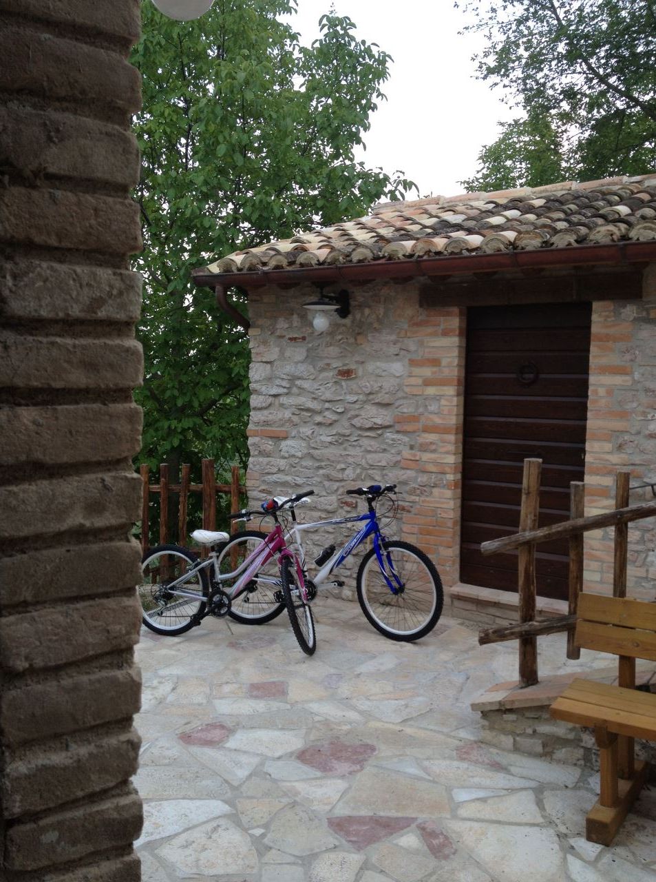 Un bâtiment en pierre avec un toit en tuiles, un banc en bois et deux vélos garés à l’extérieur.
