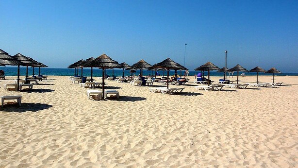 Uma praia com espreguiçadeiras e toldos de palha.