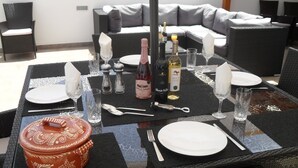 Mesa de jantar posta para quatro pessoas, com uma garrafa de vinho, saleiro e pimenteiro, abridor de garrafa e um vaso de cerâmica decorativo.