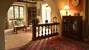 A room with a wooden table, a red patterned rug, a cabinet with glass doors, and a large window with curtains.