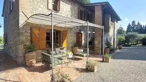 A stone building with a covered patio area featuring outdoor seating and potted plants.