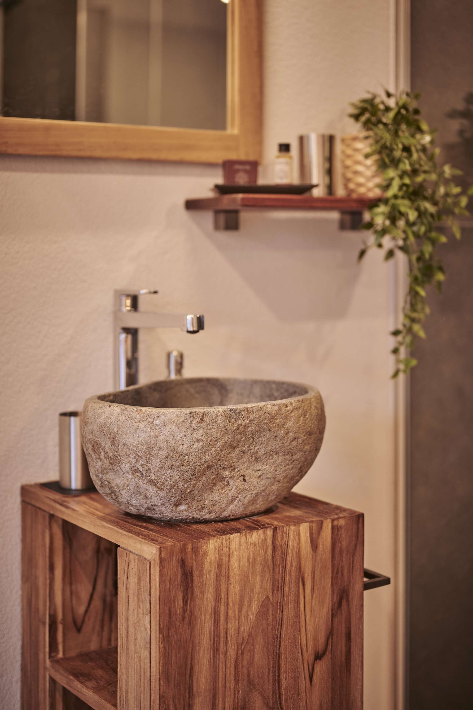 Un vasque en pierre, posé sur un piédestal en bois, dans une salle de bain avec un miroir au-dessus et une étagère contenant des articles de toilette.