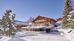 A multi-story wooden building with balconies, surrounded by snow-covered trees and a clear sky.