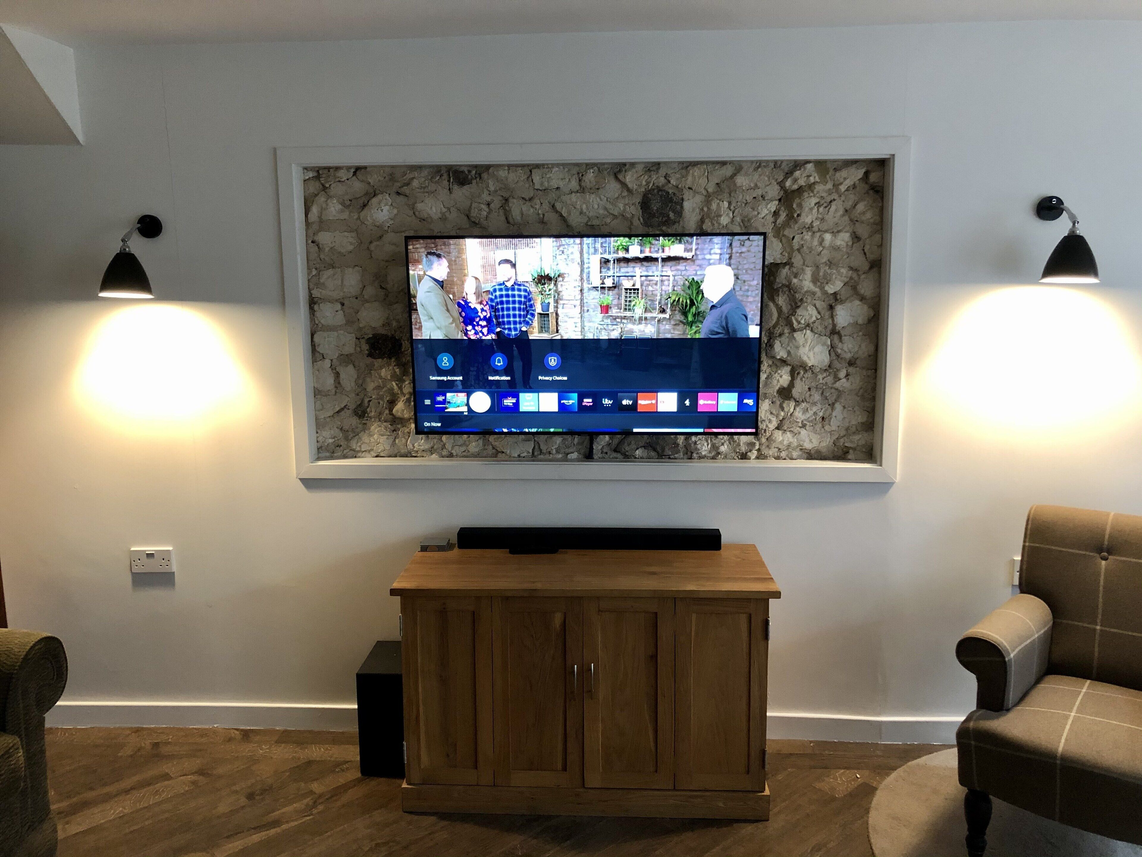 Una sala de estar con un televisor montado, un mueble de madera y dos sillones.