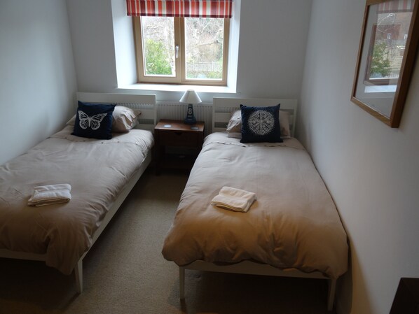A twin room with two single beds, a window with a view, a bedside table with a lamp, and a framed picture on the wall. - Once a Cattle Barn, now Spacious Luxury Accommodation! (Holme-next-the-Sea)
