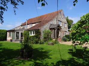 A stone house with a tiled roof, a porch, and a well-maintained lawn. - Once a Cattle Barn, now Spacious Luxury Accommodation! (Holme-next-the-Sea)