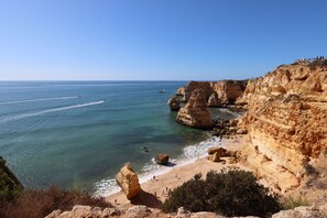 Un paysage côtier caractérisé par une falaise rocheuse, une mer d’un bleu limpide et une plage de sable.