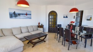 A modern living room with a sofa, coffee table, and dining area with chairs and a glass table.